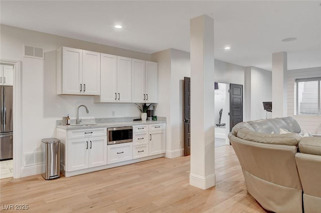 kitchen featuring stainless steel appliances, white cabinets, sink, and light wood-type flooring