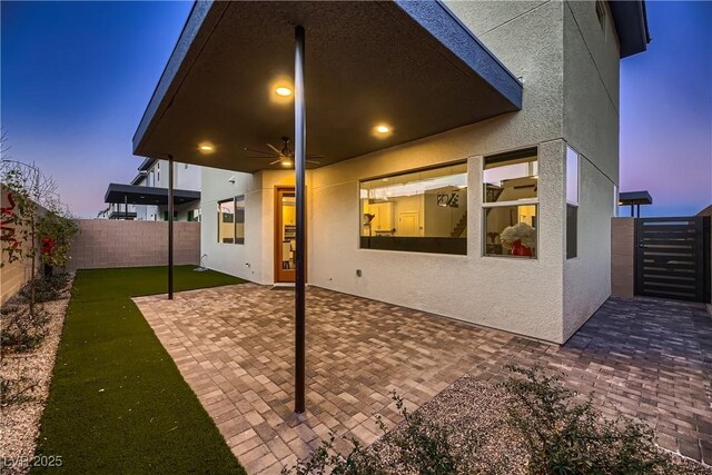 back house at dusk featuring a patio area and ceiling fan