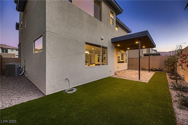 back house at dusk featuring a lawn, cooling unit, and a patio area