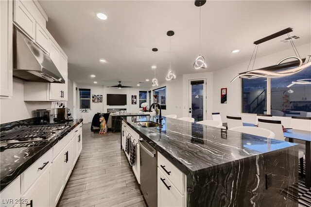 kitchen featuring white cabinets, a large island with sink, ceiling fan, dark stone counters, and sink