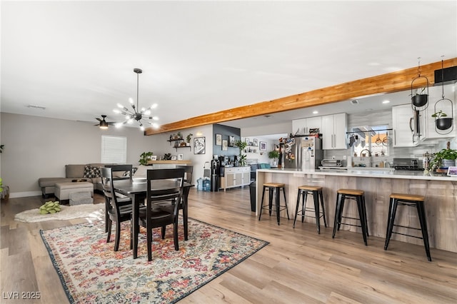 dining area featuring sink, beamed ceiling, ceiling fan with notable chandelier, and light hardwood / wood-style flooring