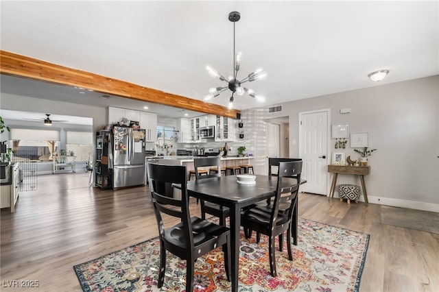 dining space with ceiling fan with notable chandelier, wood-type flooring, and beamed ceiling