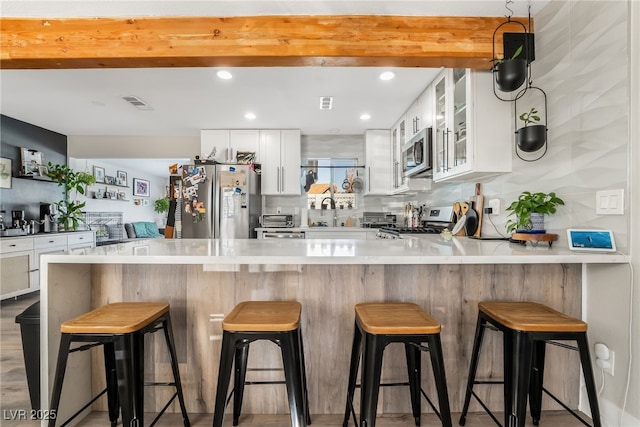 kitchen with kitchen peninsula, white cabinetry, stainless steel appliances, and a breakfast bar area