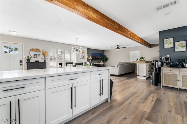 kitchen featuring beam ceiling, white cabinetry, hanging light fixtures, light wood-type flooring, and ceiling fan with notable chandelier