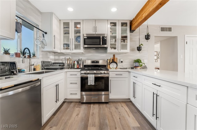 kitchen with appliances with stainless steel finishes, white cabinets, and beamed ceiling