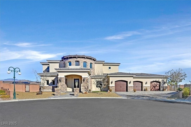 mediterranean / spanish home featuring fence, stucco siding, a garage, stone siding, and driveway