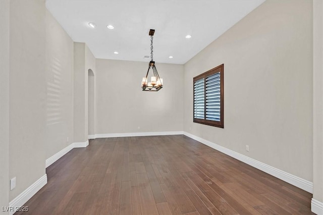 empty room with baseboards, arched walkways, an inviting chandelier, and dark wood-style floors