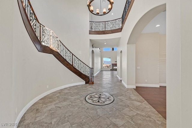 foyer entrance featuring arched walkways, a high ceiling, an inviting chandelier, baseboards, and stairs