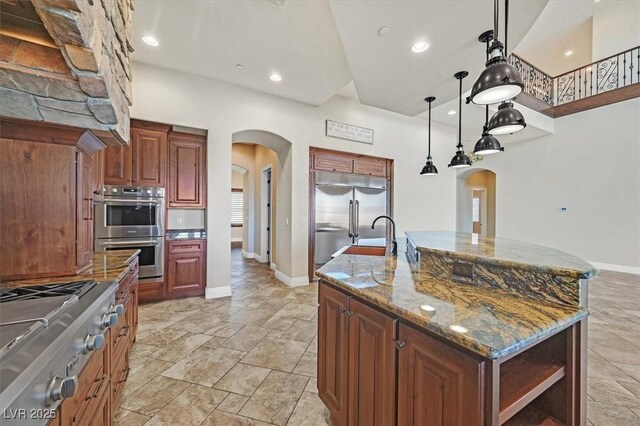 kitchen featuring sink, decorative light fixtures, a large island with sink, dark stone counters, and appliances with stainless steel finishes