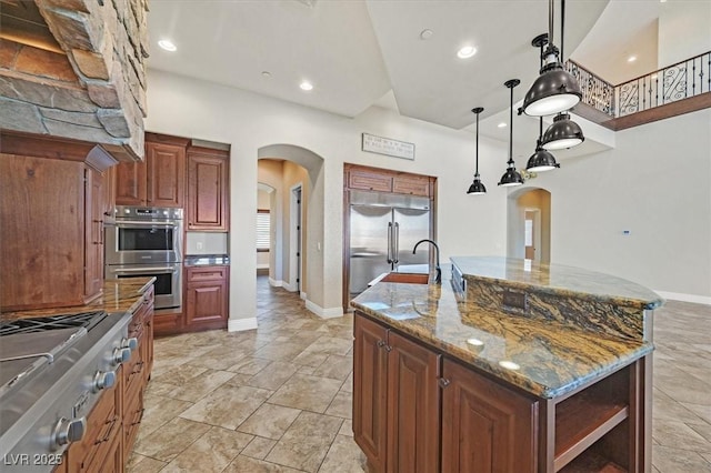 kitchen featuring a center island with sink, pendant lighting, arched walkways, stainless steel appliances, and open shelves