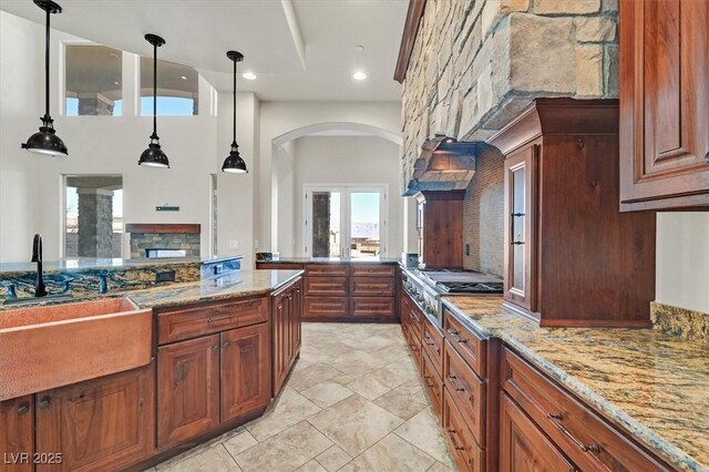 kitchen with stainless steel gas stovetop, french doors, light stone counters, sink, and decorative light fixtures