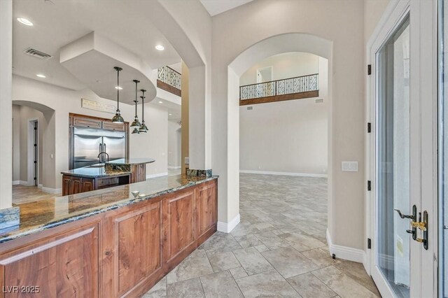 bar with dark stone counters, decorative light fixtures, and stainless steel built in refrigerator