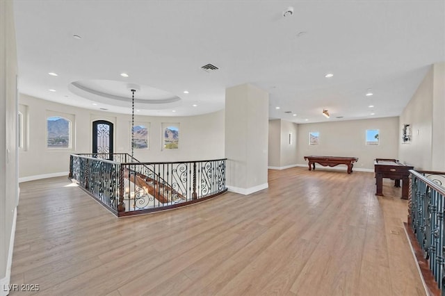 hall featuring visible vents, baseboards, an upstairs landing, light wood-style flooring, and a raised ceiling