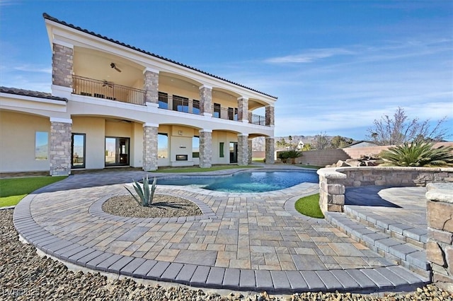 back of house with stucco siding, stone siding, a fenced in pool, a balcony, and a patio area