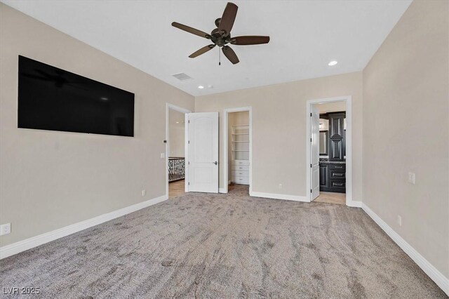 unfurnished bedroom with a spacious closet, ensuite bathroom, a closet, light colored carpet, and ceiling fan