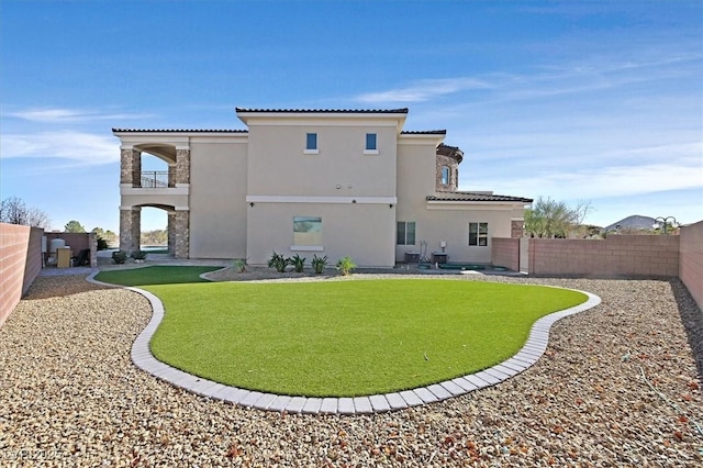 rear view of house featuring a tile roof, stucco siding, a lawn, a fenced backyard, and a balcony