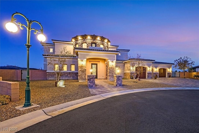 mediterranean / spanish house with fence, an attached garage, stone siding, a tiled roof, and decorative driveway