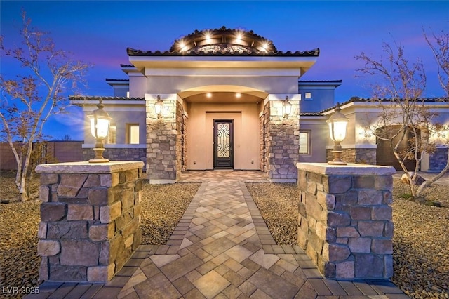 property entrance with stucco siding, stone siding, and a tile roof