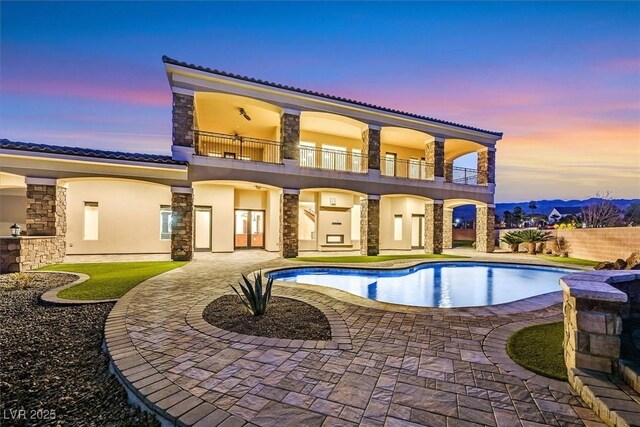 back house at dusk with a balcony and a patio