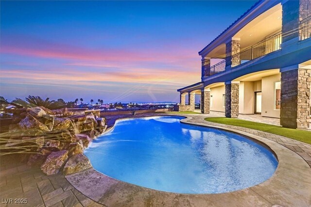 pool at dusk featuring pool water feature, a patio area, and a jacuzzi