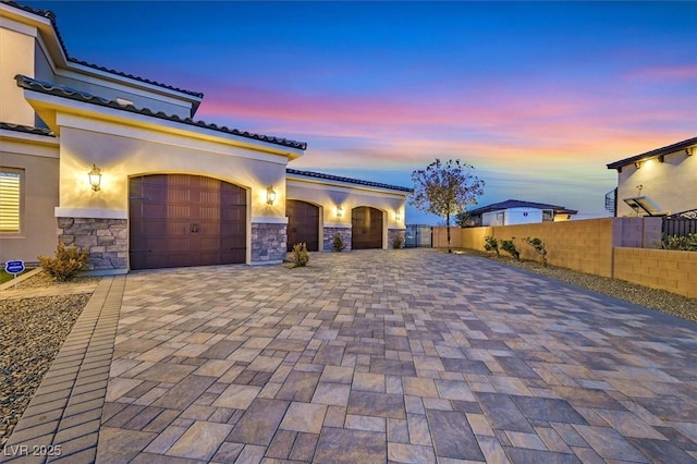 view of front of property featuring stucco siding, decorative driveway, stone siding, fence, and a garage