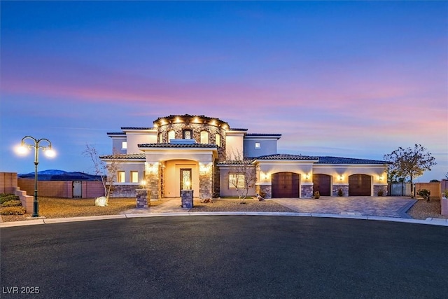 mediterranean / spanish-style home featuring stucco siding, stone siding, driveway, and a tile roof