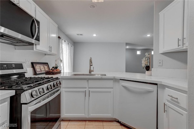 kitchen featuring stainless steel appliances, sink, white cabinetry, kitchen peninsula, and light stone countertops