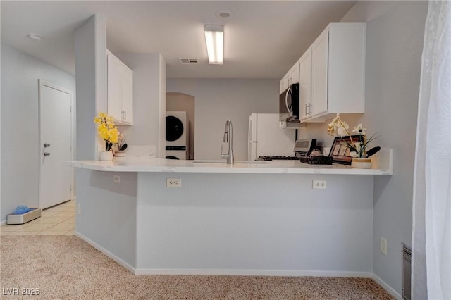 kitchen featuring kitchen peninsula, stacked washing maching and dryer, light colored carpet, and white cabinetry