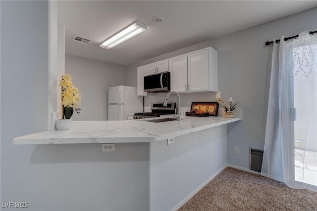 kitchen with appliances with stainless steel finishes, light colored carpet, kitchen peninsula, plenty of natural light, and white cabinets