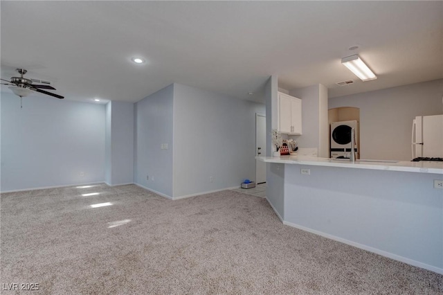 kitchen with white refrigerator, sink, white cabinets, light carpet, and stacked washer and dryer