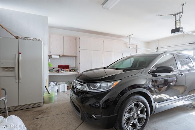 garage with a garage door opener and white refrigerator with ice dispenser