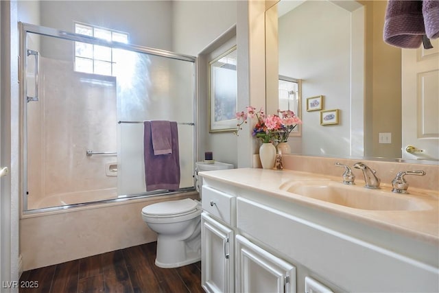 full bathroom with hardwood / wood-style floors, enclosed tub / shower combo, vanity, and toilet