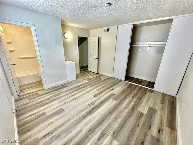 unfurnished bedroom with light hardwood / wood-style floors, ensuite bathroom, a closet, and a textured ceiling