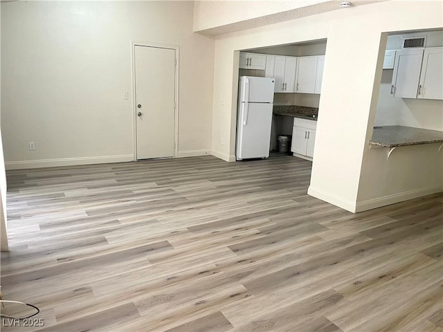 kitchen featuring light hardwood / wood-style floors, white refrigerator, white cabinetry, and dark stone counters