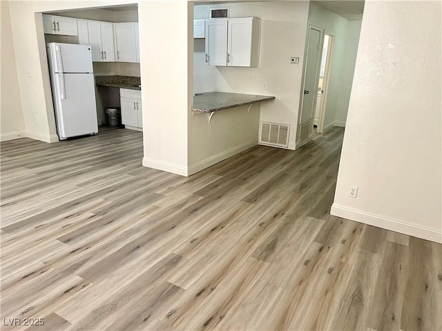 kitchen with white refrigerator, white cabinets, light hardwood / wood-style floors, and dark stone counters