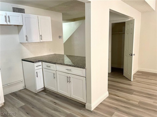 kitchen with light hardwood / wood-style floors, white cabinetry, dark stone countertops, and a textured ceiling