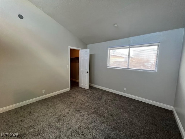 unfurnished bedroom featuring dark colored carpet, vaulted ceiling, and a spacious closet