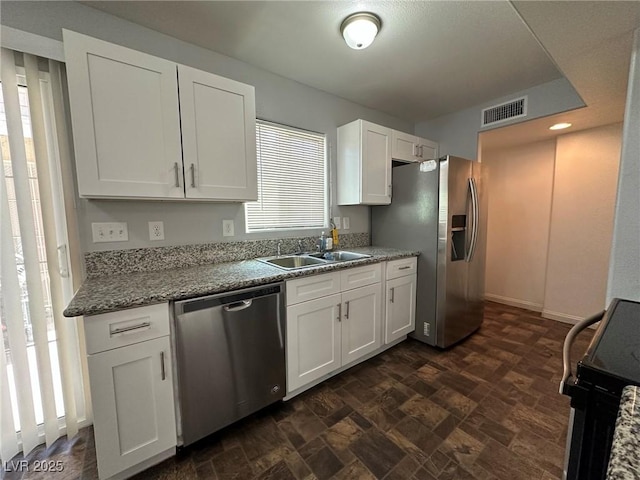 kitchen with appliances with stainless steel finishes, stone counters, a healthy amount of sunlight, sink, and white cabinetry