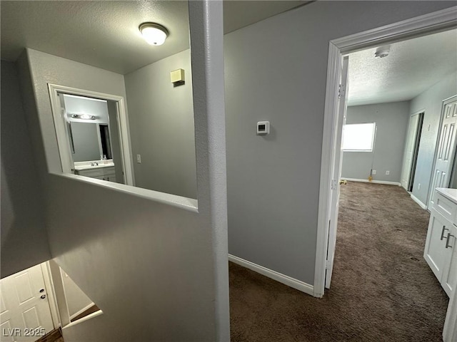 hall with a textured ceiling and dark colored carpet