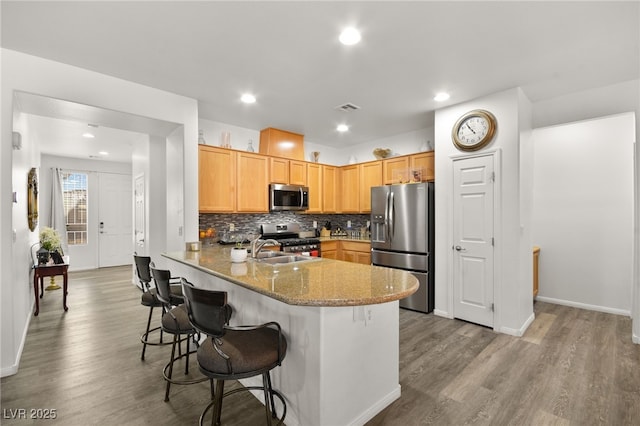 kitchen with sink, appliances with stainless steel finishes, backsplash, light stone counters, and kitchen peninsula