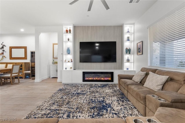 living room with light wood-type flooring, ceiling fan, a fireplace, and built in shelves