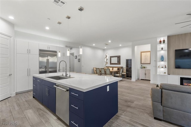 kitchen featuring pendant lighting, an island with sink, blue cabinetry, stainless steel appliances, and white cabinets