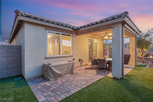 back house at dusk featuring a lawn, a patio area, and ceiling fan