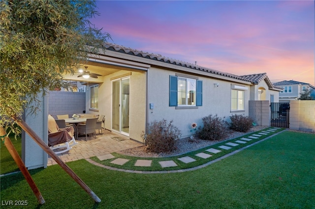 back house at dusk with a patio, ceiling fan, and a yard