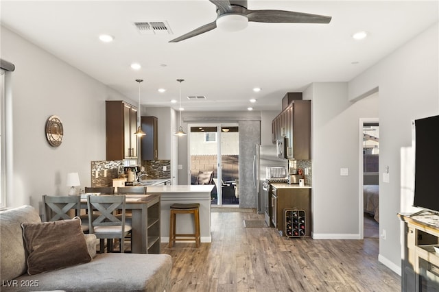 kitchen featuring a kitchen breakfast bar, hardwood / wood-style floors, kitchen peninsula, decorative light fixtures, and tasteful backsplash