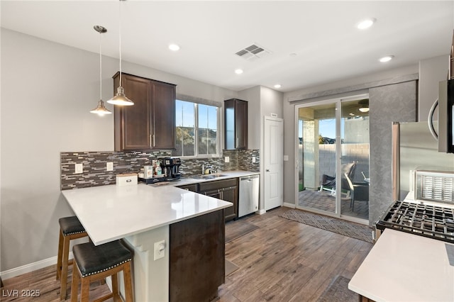 kitchen featuring kitchen peninsula, pendant lighting, stainless steel appliances, a kitchen breakfast bar, and sink