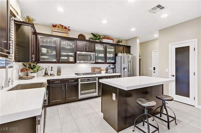 kitchen with stainless steel appliances, sink, a center island, a kitchen breakfast bar, and dark brown cabinets