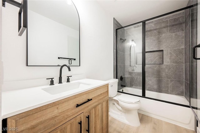 full bathroom with wood-type flooring, shower / bath combination with glass door, vanity, and toilet