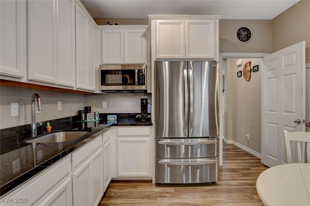 kitchen with dark stone countertops, stainless steel appliances, light wood-type flooring, white cabinets, and sink