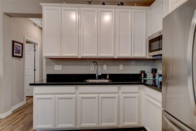 kitchen with dark stone countertops, light hardwood / wood-style floors, stainless steel appliances, sink, and white cabinetry